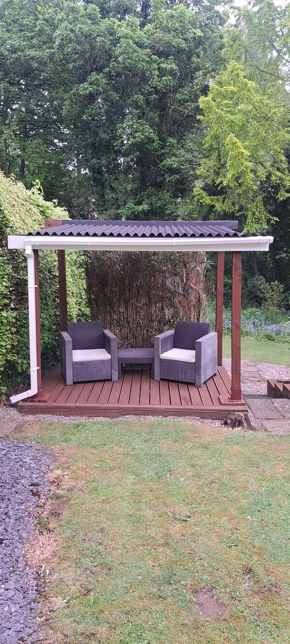 A covered patio with two wicker chairs and a wooden deck.