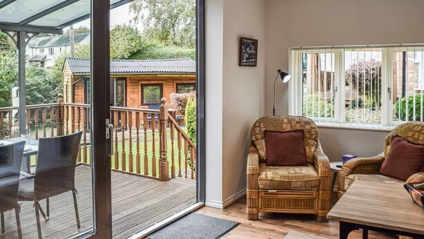 A room with a glass door leading to an outdoor deck, a wicker sofa, a wooden table, and a window with white blinds.