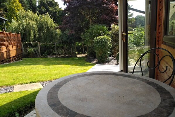 A patio with a round table and chairs, surrounded by a well-maintained garden with various plants and a wooden fence.
