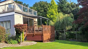 A two-story house with a covered patio, a wooden deck, and a garden with various plants and a lawn.