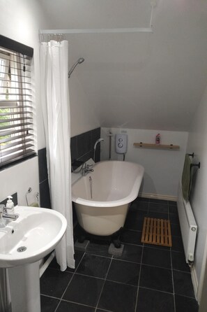 A bathroom with a bathtub, a sink, a shower curtain, a shelf with toiletries, and a window with blinds. - Luxury Private Accommodation & Hot Tub Set Within Gardens With Summer House (Manley)