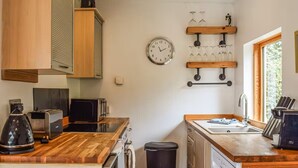 Una cocina compacta con mostradores de madera, un lavamanos, lavavajillas, cubo de basura y un reloj en la pared.