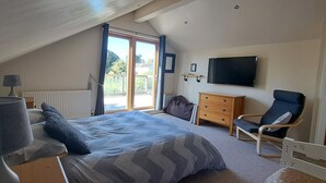 A bedroom with a bed, a chair, a TV, a dresser, and a window with a view.