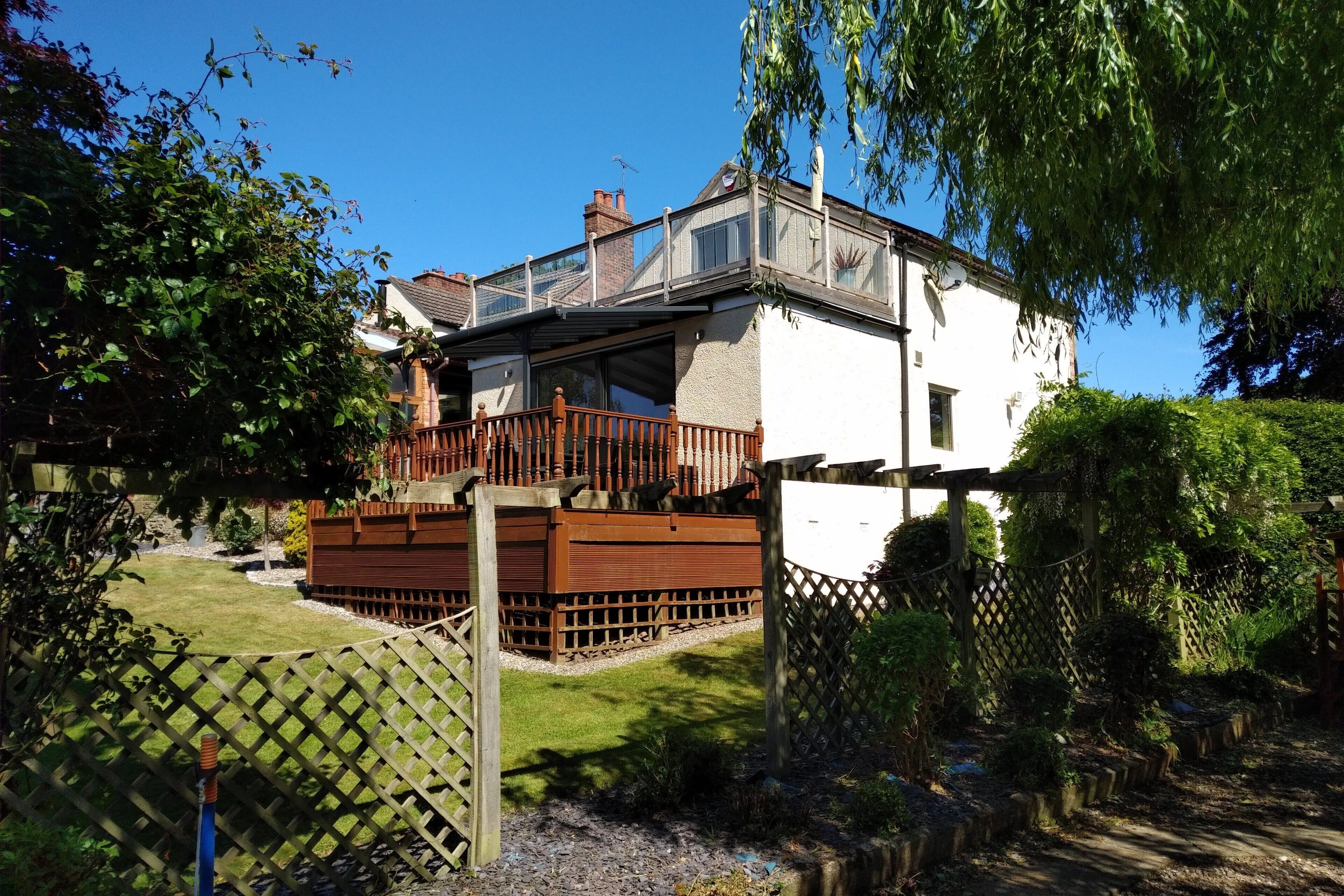 A two-story house with a wooden deck and a fenced garden.