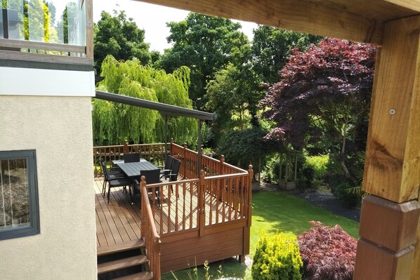 A wooden deck with a table and chairs, surrounded by lush greenery and trees. - Luxury Private Accommodation & Hot Tub Set Within Gardens With Summer House (Manley)