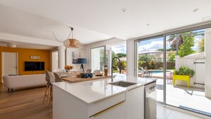 Een moderne keuken met een groot eiland, een eethoek met een tafel en stoelen, een bank en een televisie.