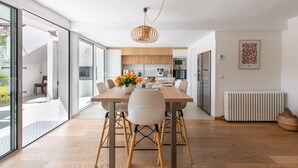 Een moderne keuken met houten kastjes, een eettafel met stoelen en een hangende lamp.