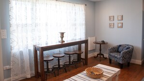 A room with a wooden bar stool set, a patterned armchair, and a white table with a basket.