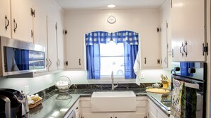 A kitchen with white cabinets, a black countertop, a sink, a coffee maker, and a window with blue curtains.