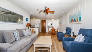 A living room with a grey sofa, blue armchairs, a wooden coffee table, and a dining area with a table and chairs.