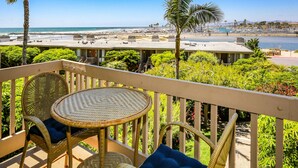 Un balcón con sillas de mimbre y una mesa con vistas a una playa y un puerto deportivo.