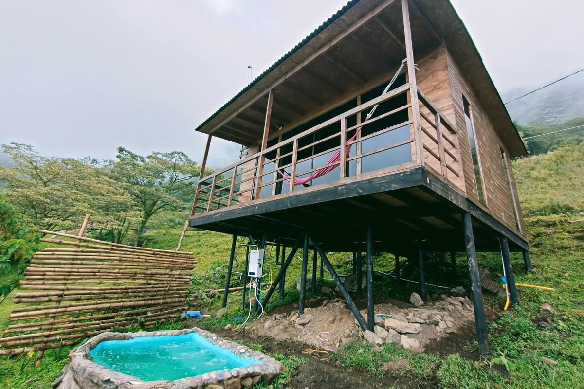 Una cabaña de madera con balcón, una piscina pequeña y un entorno natural.