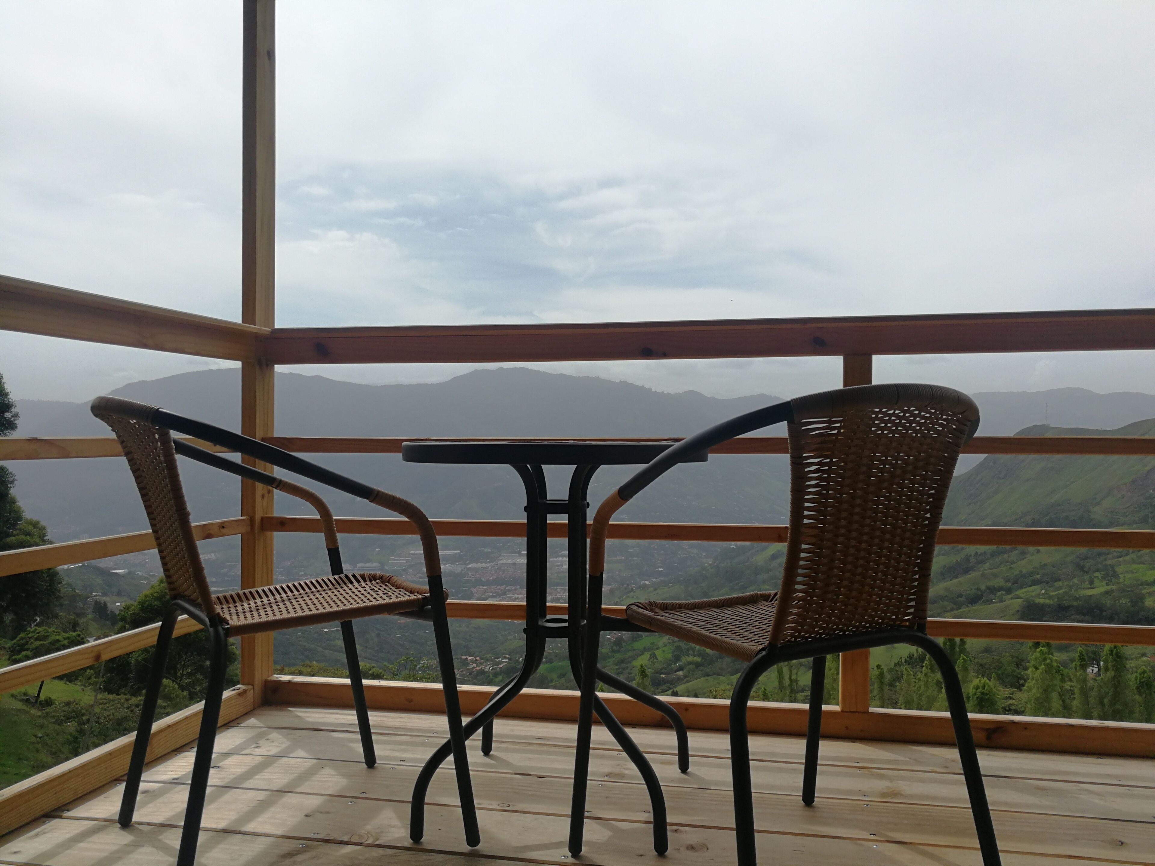 A balcony with two wicker chairs and a small table, overlooking a mountainous landscape.