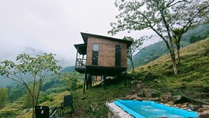 Una cabaña de madera con un balcón, una piscina pequeña y una silla.