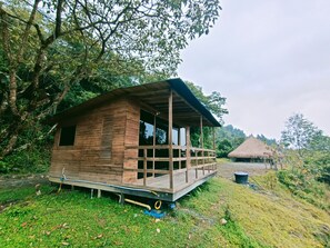 A wooden cabin with a porch, surrounded by lush greenery and trees. - Reserva Tororoi (Copacabana)