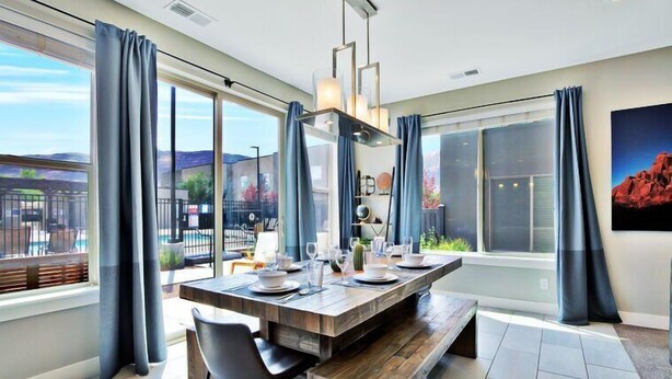 A modern dining area with a wooden table set for four, large windows with curtains, and a view of the outdoors. - Entrada at Moab 619 and 623 | Townies | Pool/Spa | Garage | Same Day Booking (Moab)
