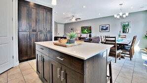 A modern kitchen with dark wood cabinets, a large island, pendant lighting, and a dining area with wooden chairs and a table. - Entrada at Moab 619 and 623 | Townies | Pool/Spa | Garage | Same Day Booking (Moab)