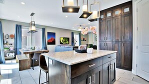 A modern kitchen with dark wood cabinets, a marble island, pendant lighting, and a dining area with a blue couch and a table set for four. - Entrada at Moab 619 and 623 | Townies | Pool/Spa | Garage | Same Day Booking (Moab)