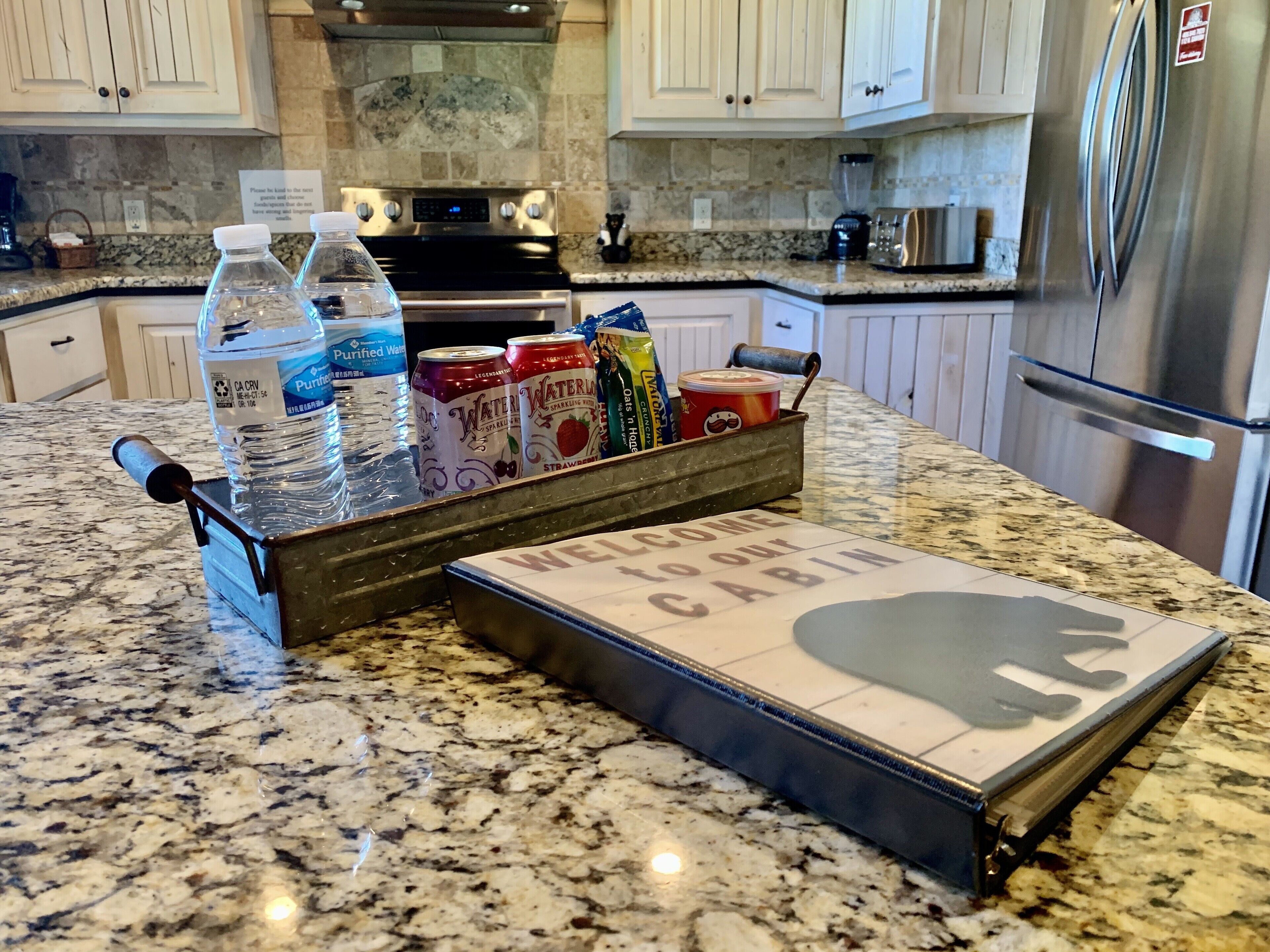 A kitchen counter with a water dispenser, a coffee maker, and a sign that reads "Welcome to our Cabin."