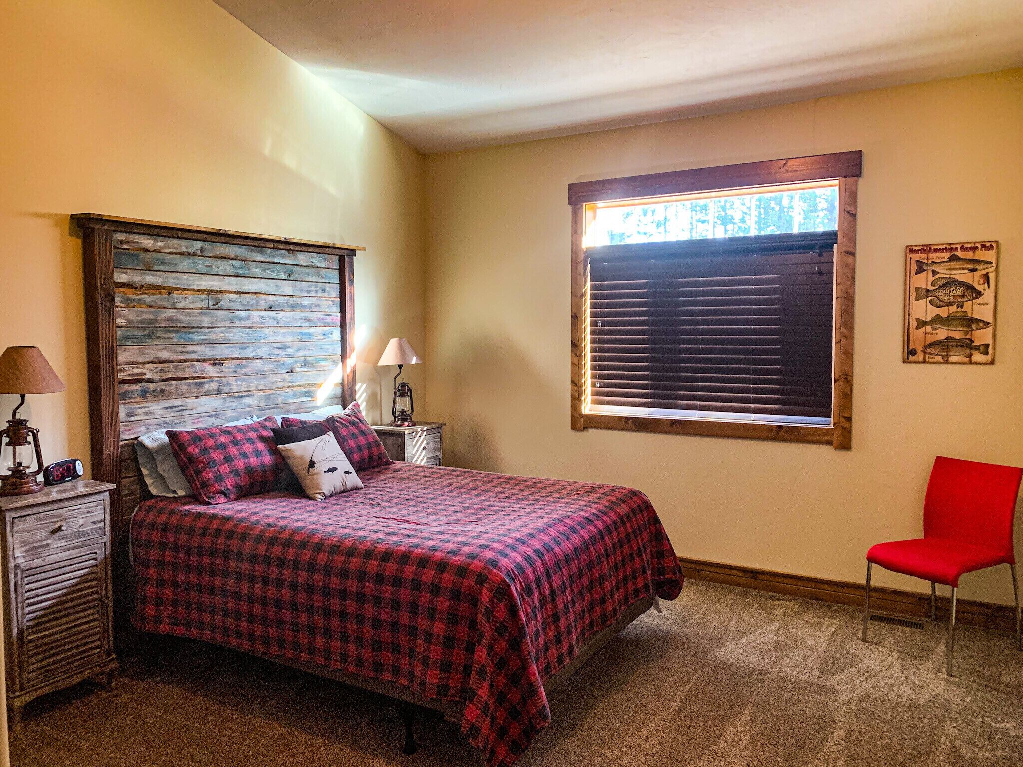 A bedroom with a bed, a nightstand, a lamp, a chair, and a window with blinds.
