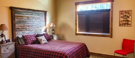 A bedroom with a bed, a nightstand, a lamp, a chair, and a window with blinds.