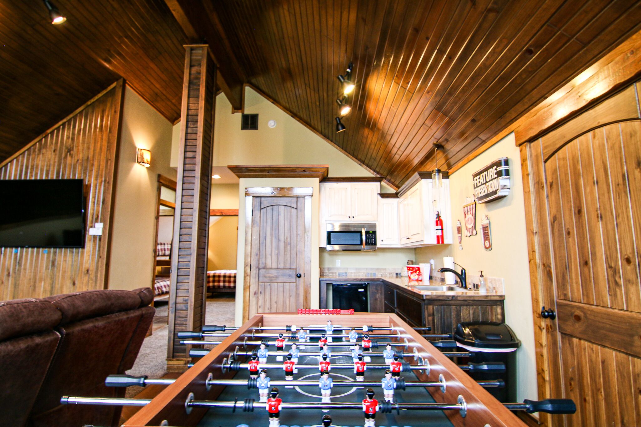 A foosball table in a room with wooden walls and a kitchen area visible in the background.