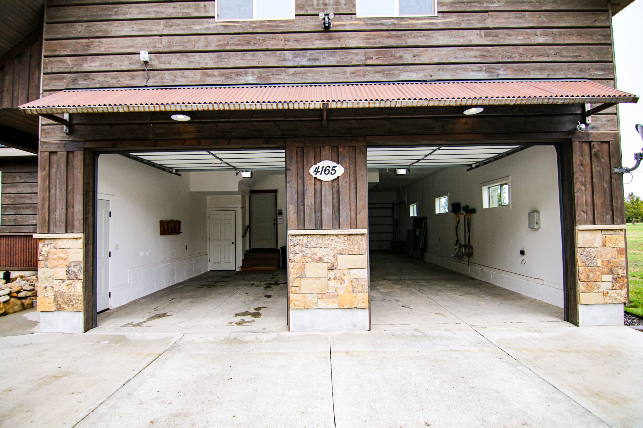 A covered garage entrance with a stone and wood facade, a number sign, and a clean concrete floor.