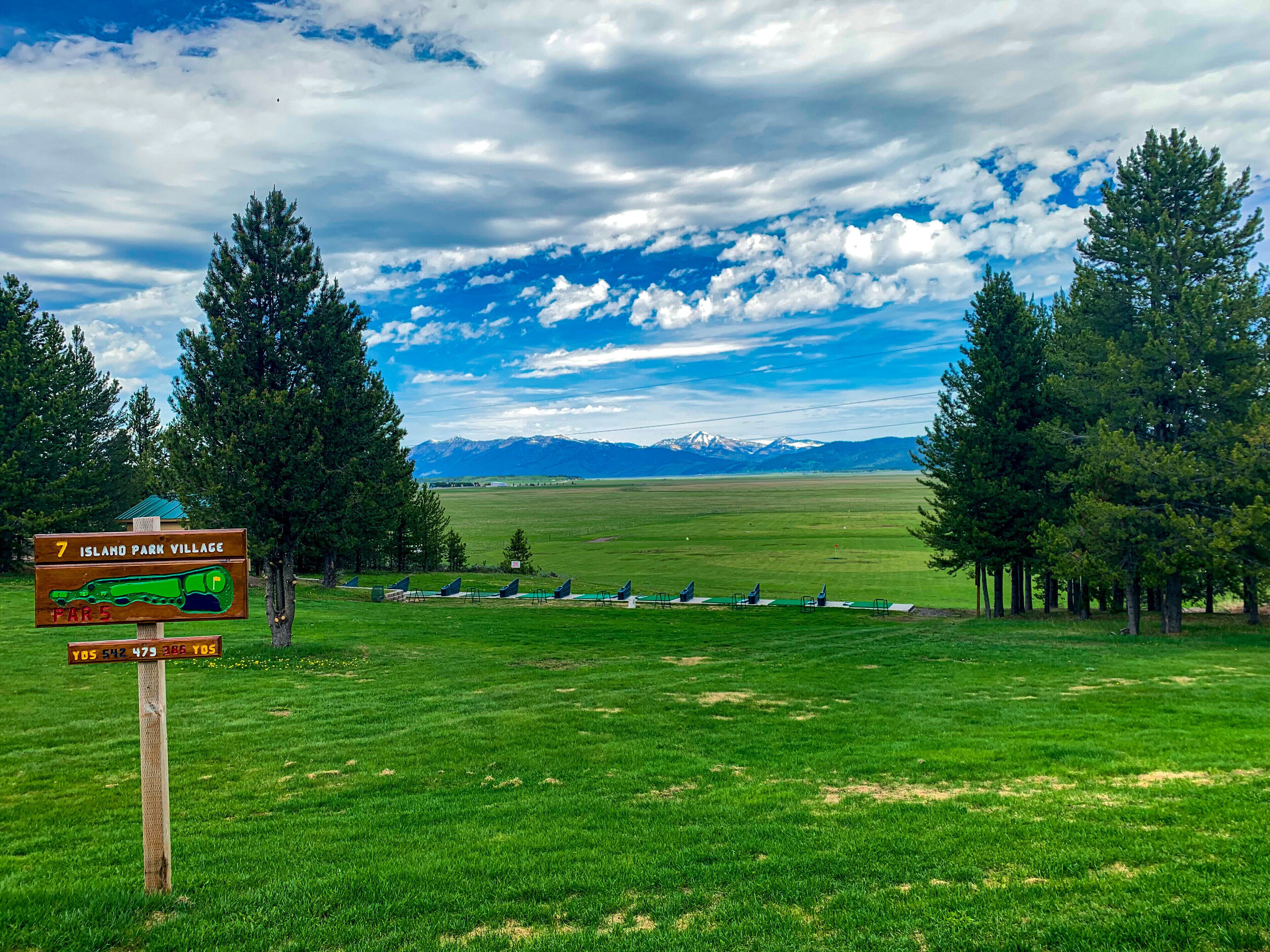 A sign for Island Park Village with a view of mountains in the distance.