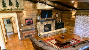 A cozy living room with a stone fireplace, leather sofa, and a television. - Luxury Cabin,Golf Course,Yellowstone, Stunning Mountain Views,Tubing, Rafting, (Island Park)