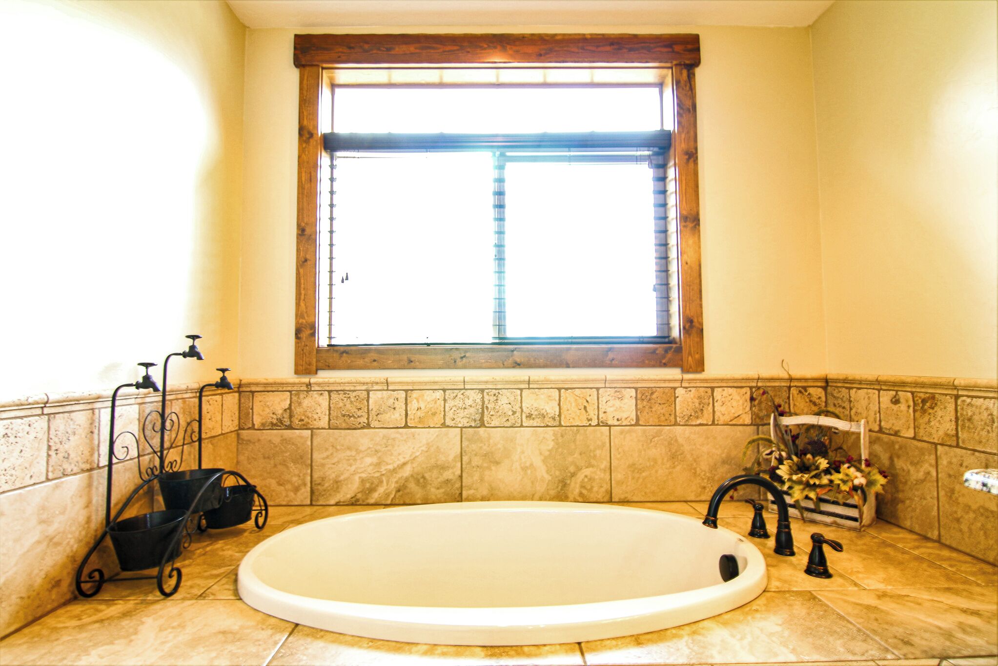 Une salle de bain avec une grande baignoire, une fenêtre avec des stores et un sol carrelé.