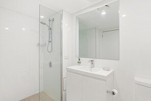 Een moderne badkamer met een douchecabine van glas, een witte wastafel en een grote spiegel.