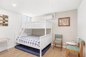 Een stapelbed met een bureau en stoelen, een bijzettafeltje en een schilderij aan de muur.