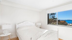 Enjoy a serene coastal view from the large window in this stylish bedroom, featuring a comfortable white bed and a minimalist design.