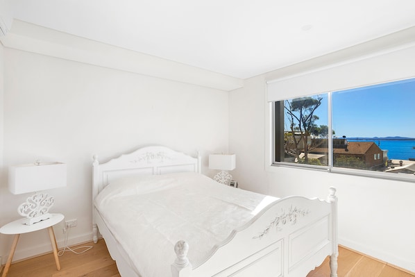 A bedroom with a bed, bedside tables, a window with a view of the sea, and a small round table.