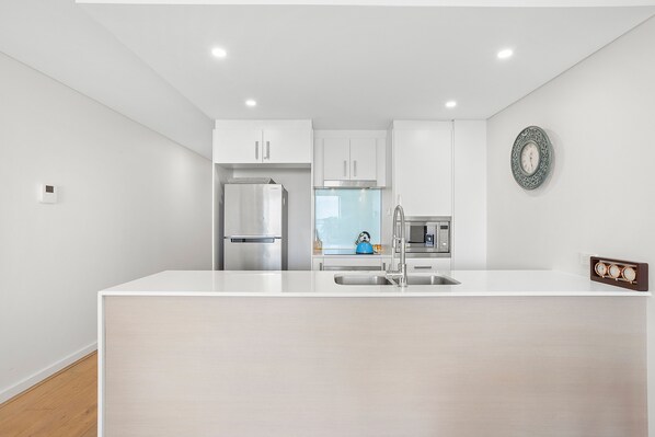 A modern kitchen with white cabinetry, stainless steel appliances, and a central island with a sink. - The Shoal Apartment 310 Coastal Escape with Views (Shoal Bay)