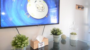 Un televisor mostrando un personaje de dibujos animados, una caja de pañuelos y tres macetas con plantas sobre una mesa.