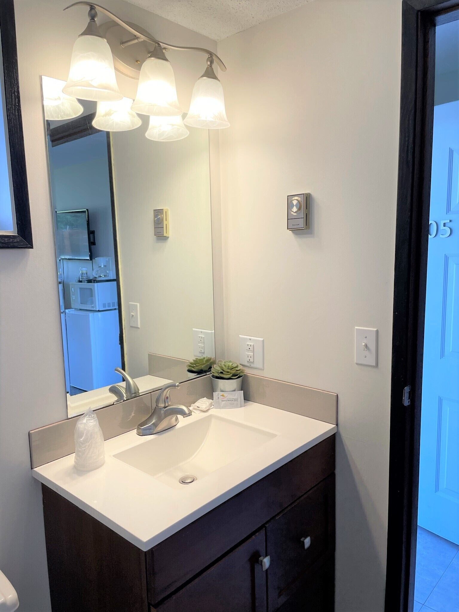 A bathroom with a white sink, dark cabinets, a large mirror, and three pendant lights.