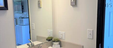 A bathroom with a white sink, dark cabinets, a large mirror, and three pendant lights.