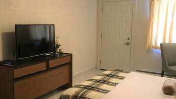 A bedroom with a bed, a TV on a wooden dresser, a door, and a window with curtains.