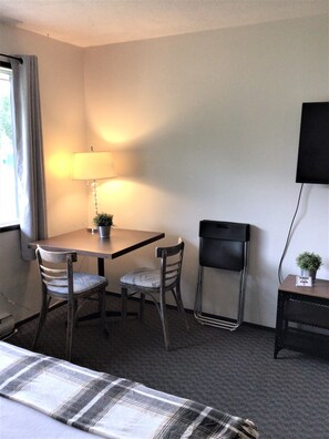A hotel room with a bed, a table with two chairs, a lamp, a TV, and a small plant on a side table. - Christina Lake Motel and RV Park (Christina Lake)