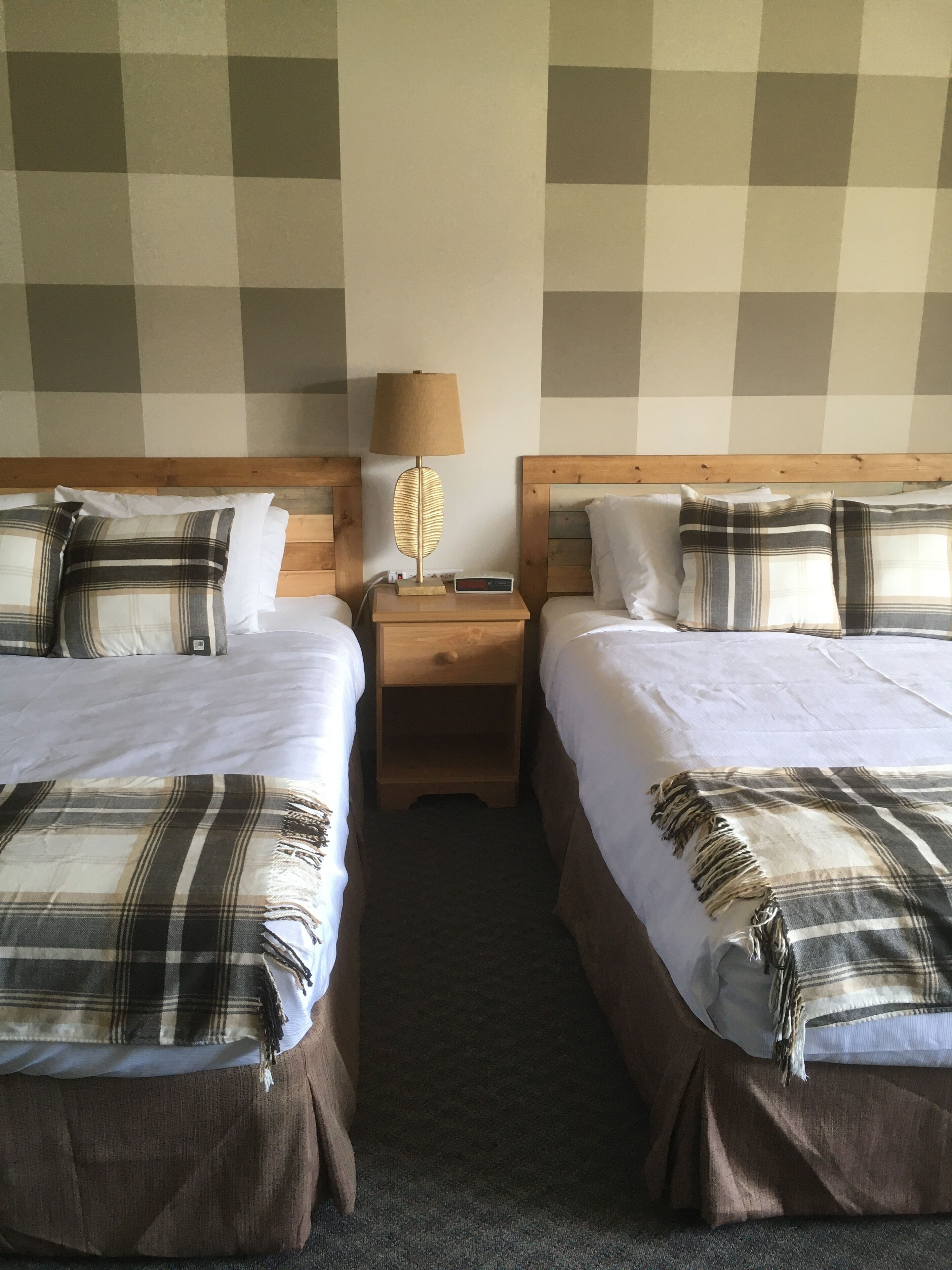A hotel room with two beds, a nightstand, a lamp, and a digital clock.