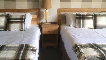 A hotel room with two beds, a nightstand, a lamp, and a digital clock.