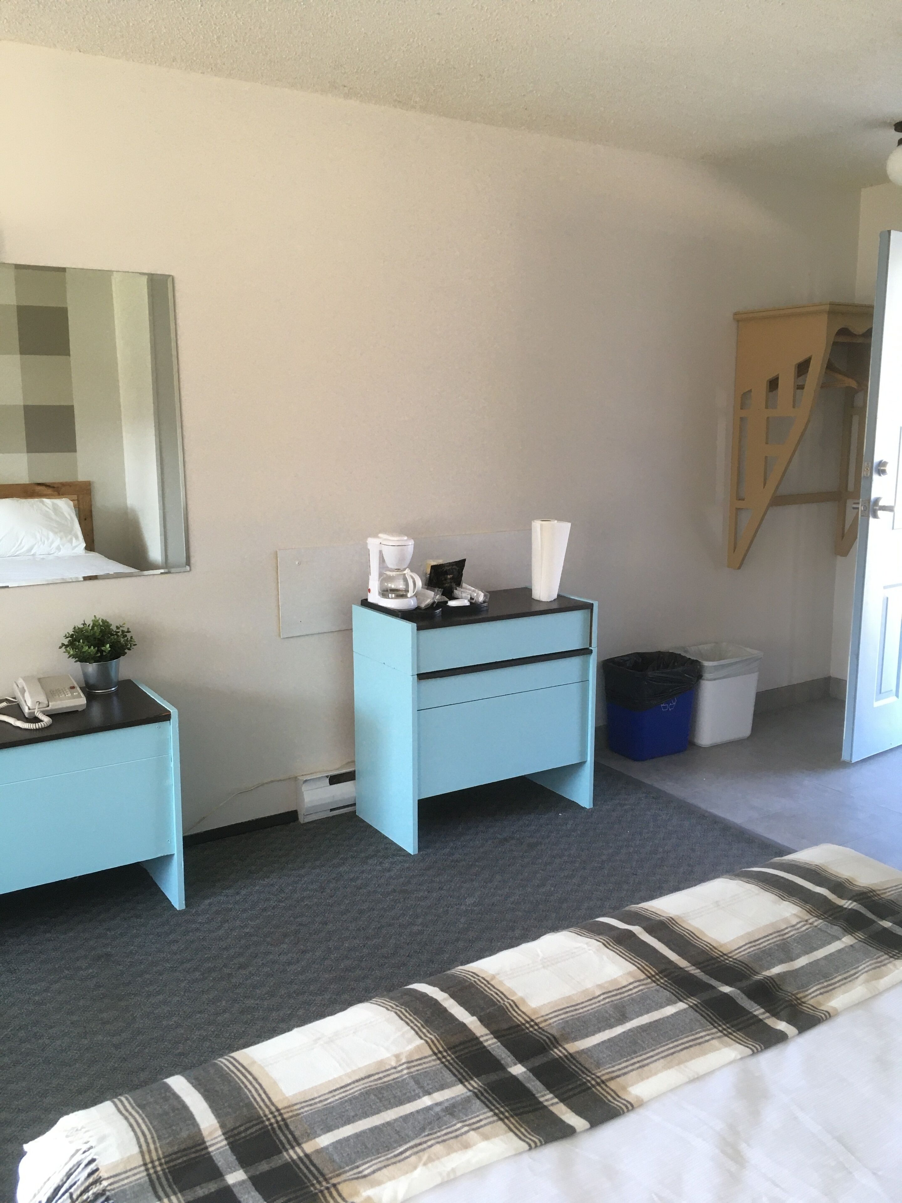 A bedroom with a bed, a nightstand, a dresser, a mirror, a window, and a door.