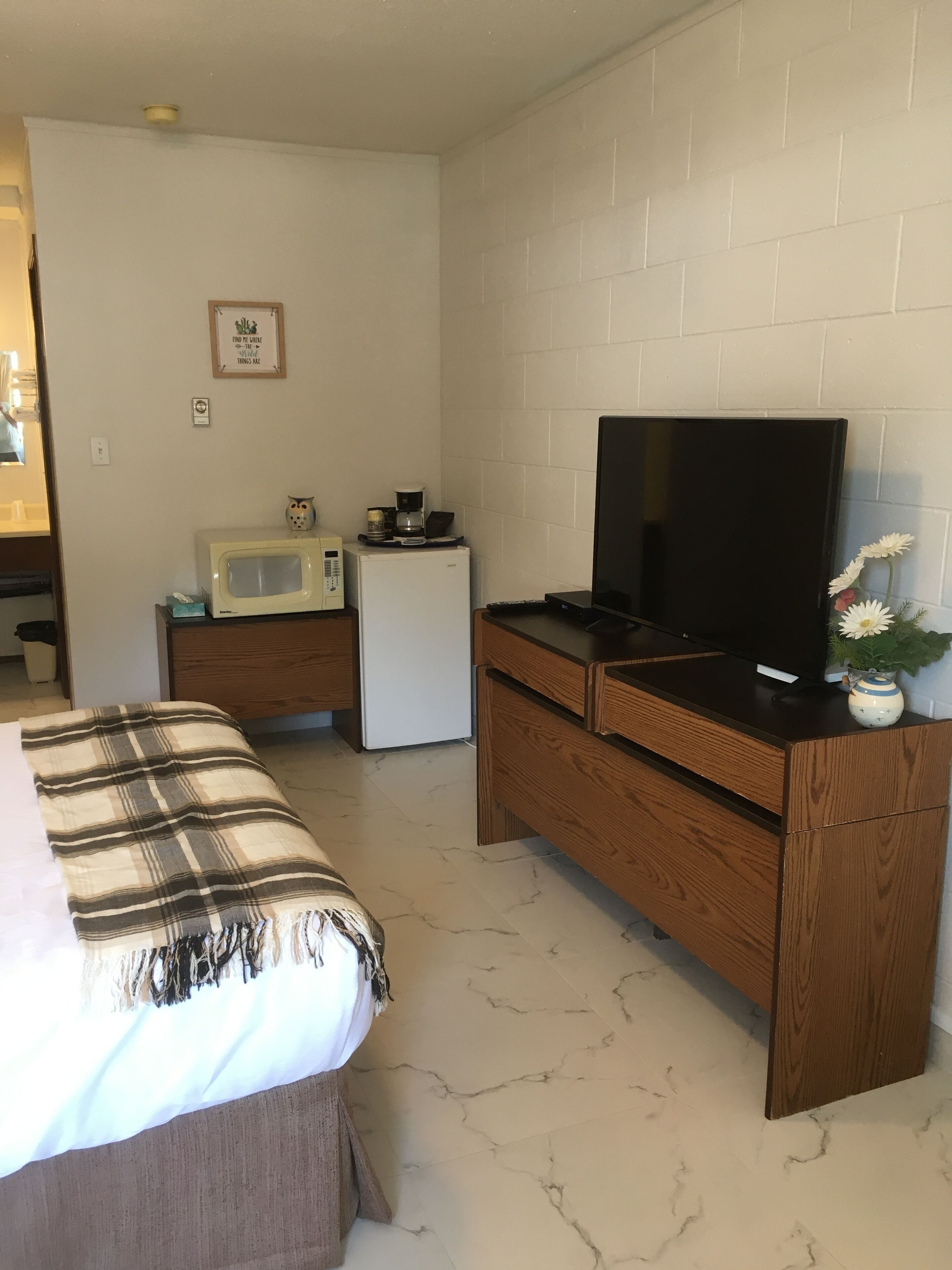 A bedroom with a bed, a wooden dresser, a television, a microwave, and a refrigerator.