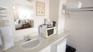 Un baño con lavamanos, espejo, microondas y barra para toallas.
