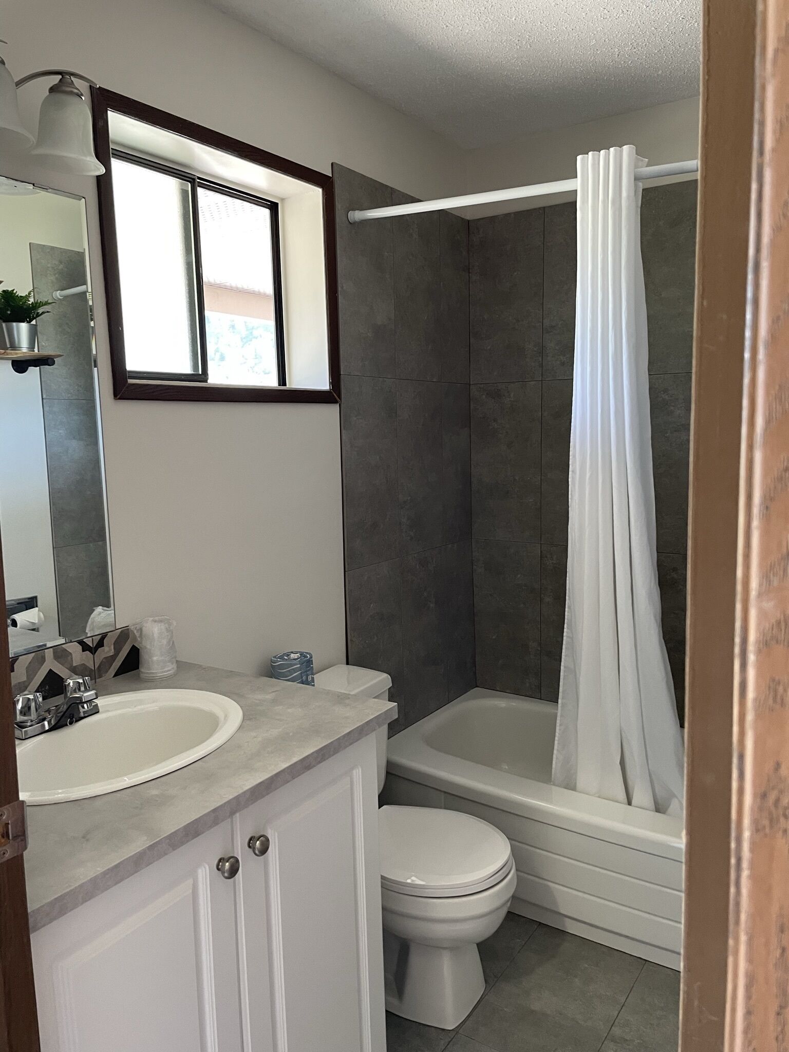 A bathroom with a white sink, toilet, and bathtub. There is a window above the sink and a shower curtain.