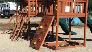 Un parque infantil con muros de escalar y toboganes, rodeado de una zona de arena con una bandera al fondo.