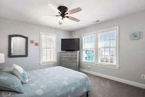 A bedroom with a bed, dresser, television, and large windows. - 5 Buoys: Ocean View House Near Ocean Crest Pier (Oak Island)
