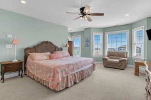 A bedroom with a bed, a chair, a nightstand, a lamp, and a ceiling fan. - 5 Buoys: Ocean View House Near Ocean Crest Pier (Oak Island)