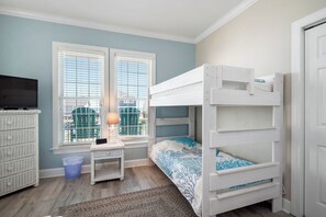 A bedroom with a bunk bed, a television, a wicker dresser, and a window with blinds.
